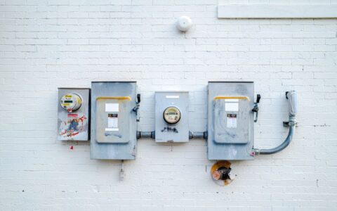 Electrical boxes and power meters mounted on a white brick wall.