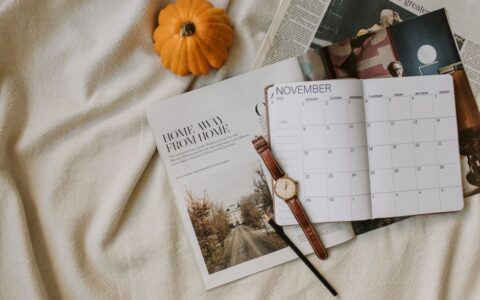 Flat lay of a November calendar, watch, and pumpkin reflecting cozy autumn planning vibes.