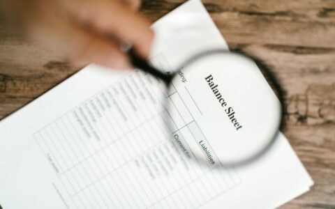 Close-up of a balance sheet under a magnifying glass on a wooden table.