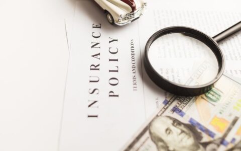 Close-up image of an insurance policy with a magnifying glass, money, and toy car.