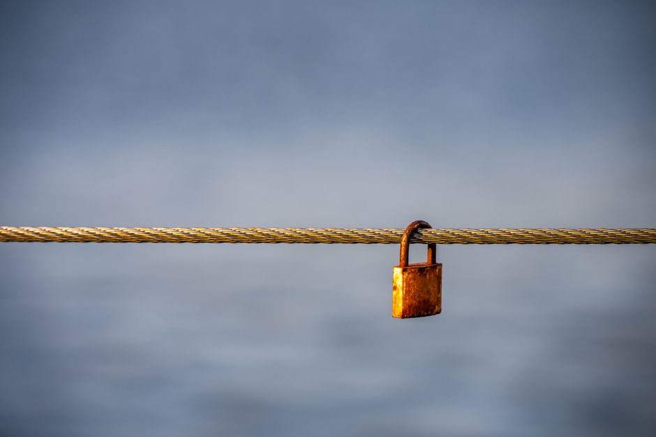 A rustic padlock secured to a sturdy cable set against a peaceful blue background. Ideal for themes of security.