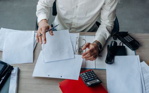 A business professional organizing documents at a busy office desk, emphasizing productivity.