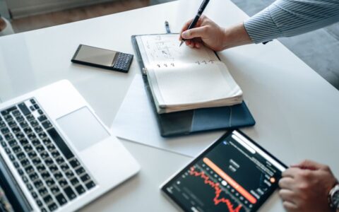 Person analyzing financial data on laptop, tablet, and notebook.