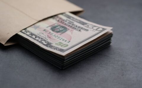 Close-up of US fifty dollar bills partially enclosed in a brown envelope, symbolizing finances.