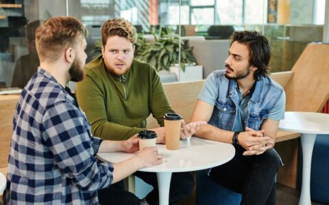 Three men having a casual business meeting in a cafe, engaging in conversation over coffee.
