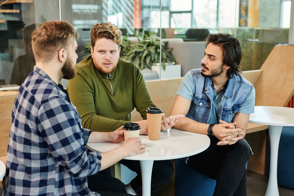 Three men having a casual business meeting in a cafe, engaging in conversation over coffee.